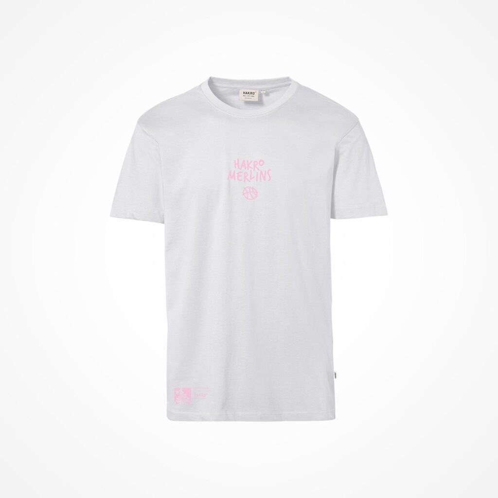 Ein schlichtes weißes T-Shirt mit kurzen Ärmeln, auf dessen Vorderseite ein rosa Schriftzug und eine kleine Grafik mit der Aufschrift „HAKRO MERLINS“ zu sehen sind. Das Shirt ist vor einem weißen Hintergrund abgebildet.